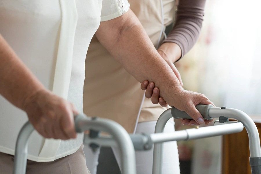 Old person with walking aid helped by nurse